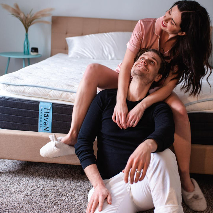 Couple smiling smiling sitting at the foot on a Haven Mattress with Haven Mattress tag showing