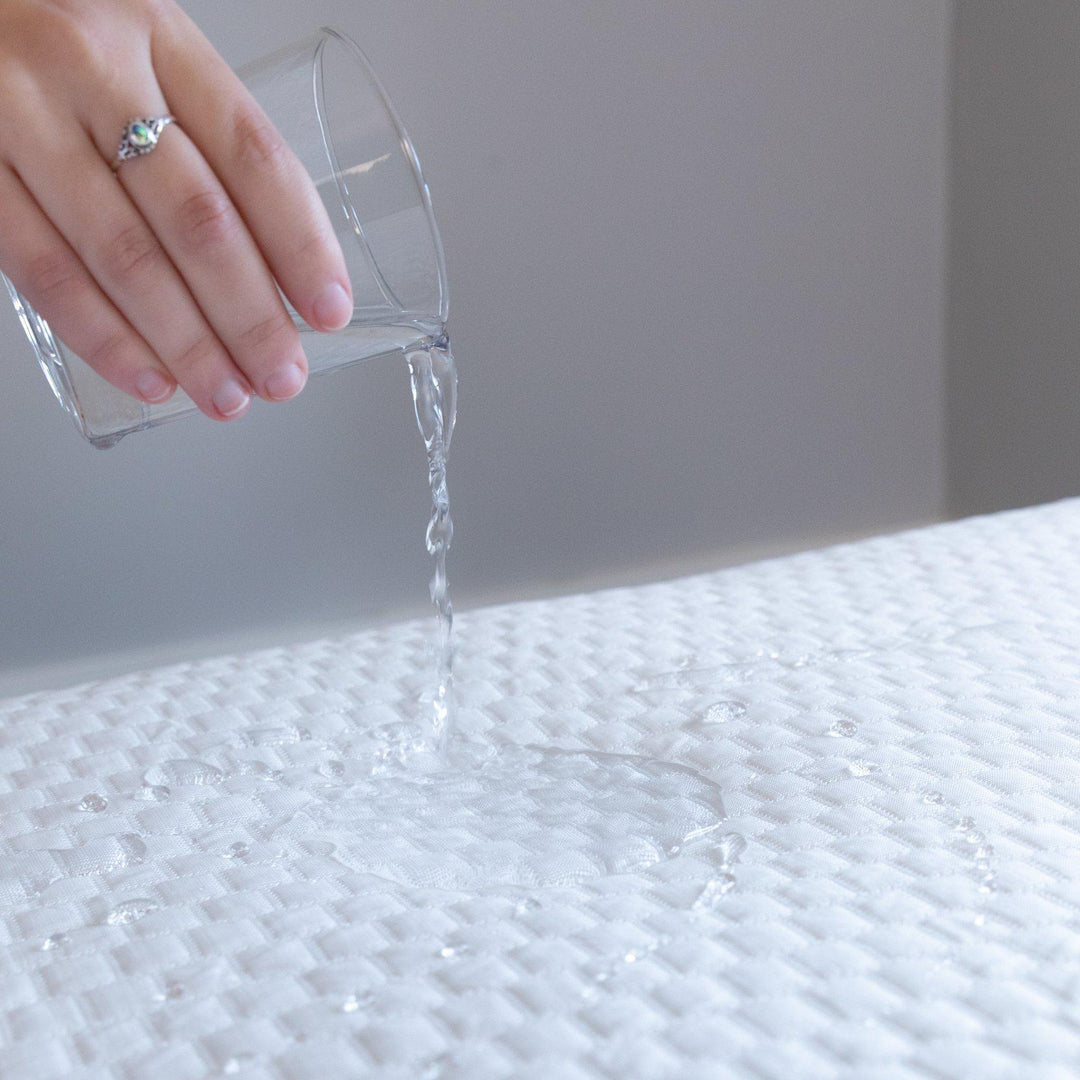 Close up of a hand pouring a glass of water onto a Bedface Artic Cooling Mattress protector showing the protector is waterproof