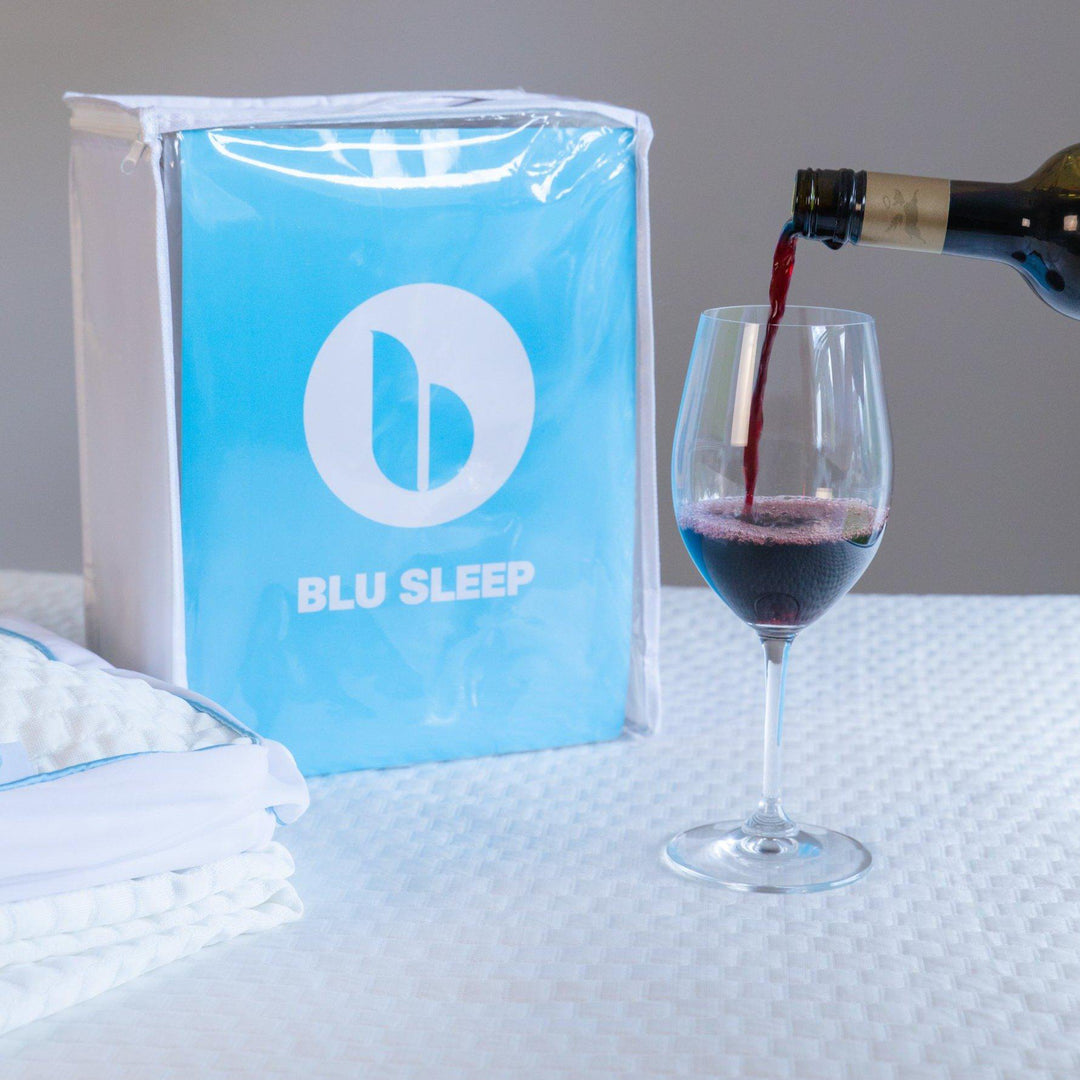 close up of a Bedface Artic Cooling Mattress Protector in packaging sitting on top of a Haven Mattress with a glass of red wine being poured beside it to showcase the safety of the mattress protector