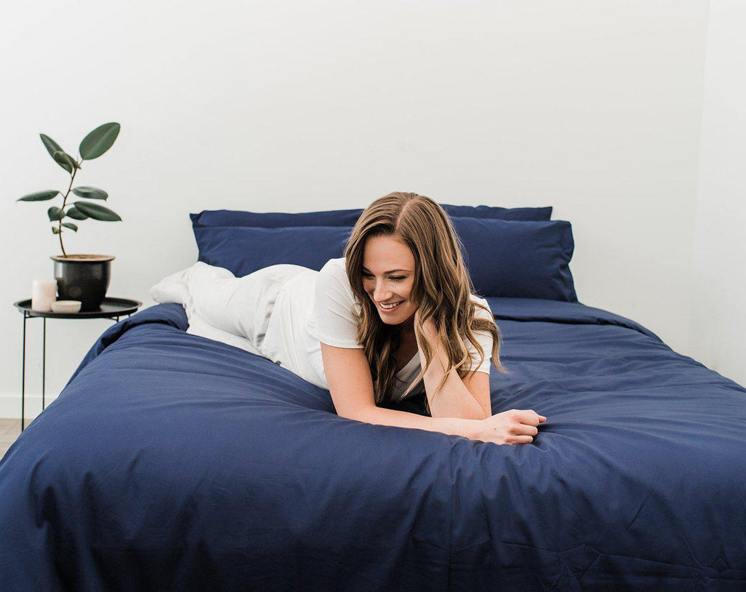 Woman in white laying across Haven Mattress with Nighttime Navy Blue bedding