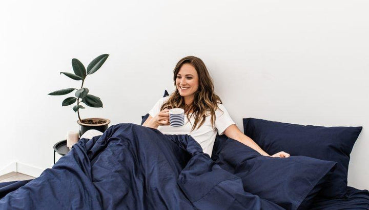 woman in white tucked into Bedface 100% cotton Percale sheet set and Duvet cover in nighttime navy blue