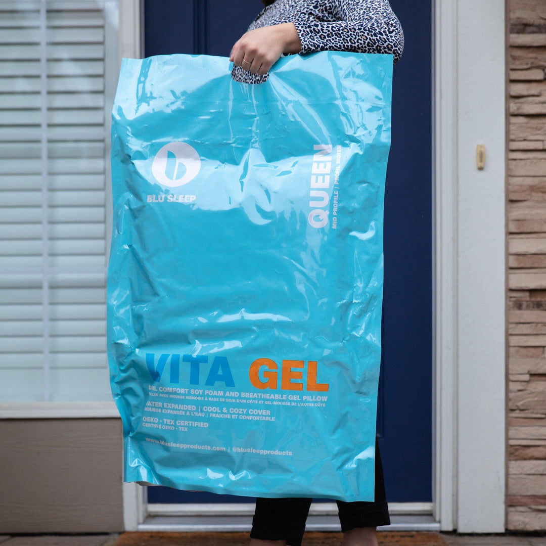 Woman carrying a Blu Sleep Bedface VitaGel 4 in 1 pillow bag with Blu Sleep logo. It says Queen down the side and Vita Gel across front with details of the Pillow on bag