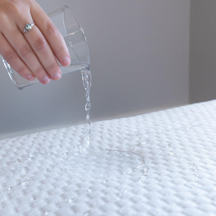 Close up of a hand pouring a glass of water onto a Bedface Artic Cooling Mattress protector showing the protector is waterproof