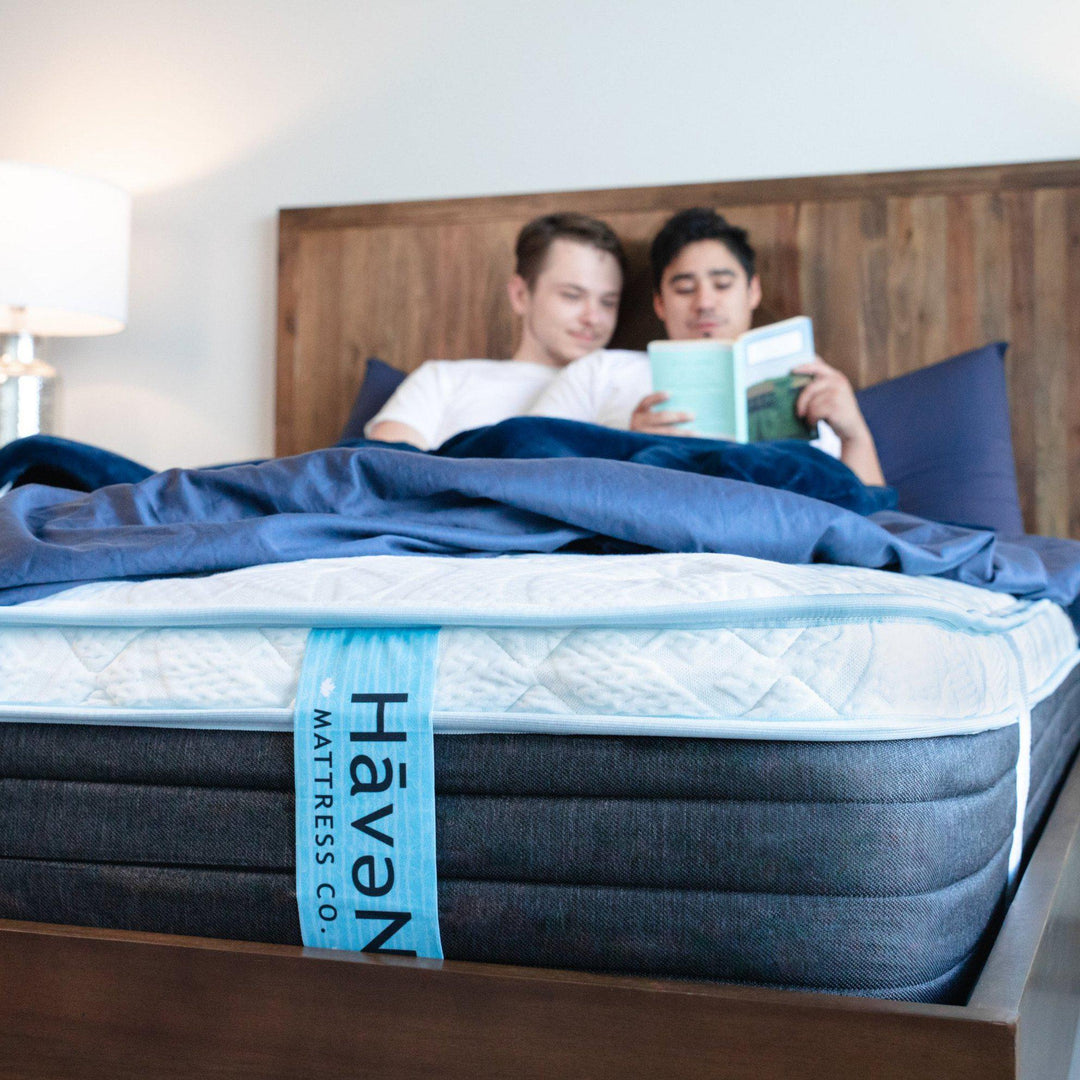 couple laying in bed reading a book together tucked into Nighttime Navy Bedface Sheets. Bottom sheet is folded up to show the Haven Mattress tag down front