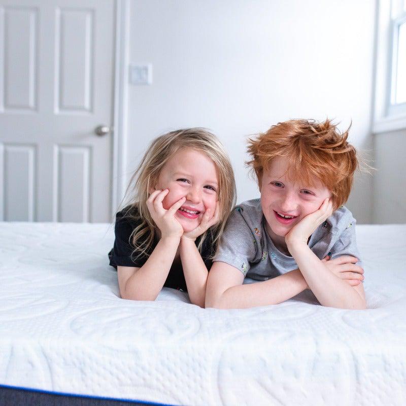 cute red haired boy and blonde girl with hands tucked under chin smiling while laying across on a 10" rejuvenate haven lux rejuvenate springwall chiropractic mattress 