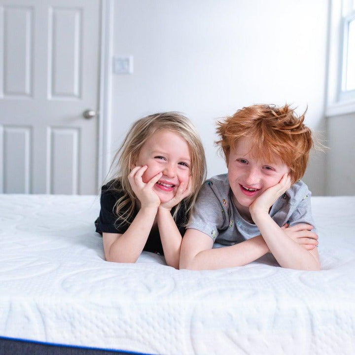 cute red haired boy and blonde girl with hands tucked under chin smiling while laying across on a 10" rejuvenate haven lux rejuvenate springwall chiropractic mattress 