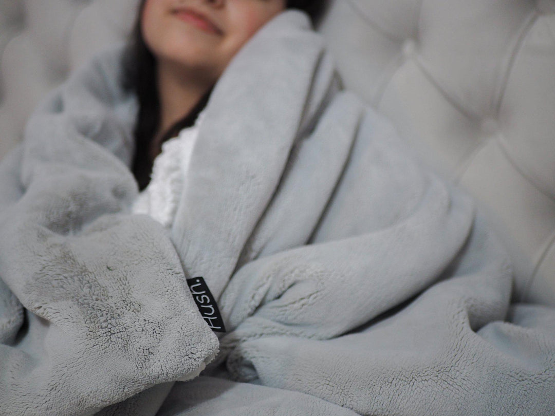Waman wrapped up in a Hush weighted throw in grey with Hush label tag showing