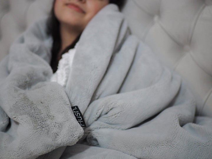 Waman wrapped up in a Hush weighted throw in grey with Hush label tag showing