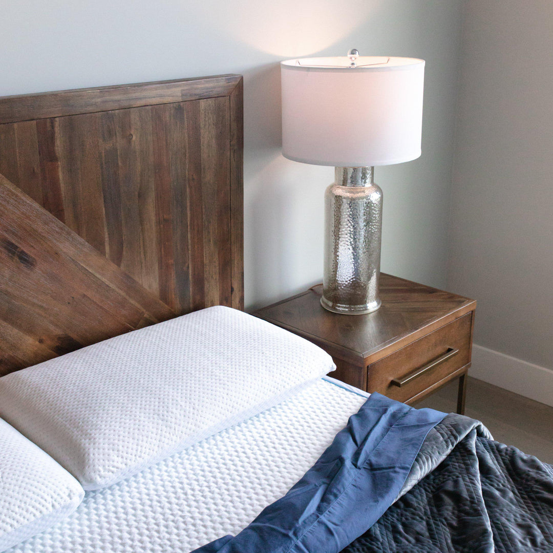 showcase of Bedface Artic Cooling Pillow protector and mattress protector covering a memory foam pillow and Haven Mattress with blue bedding folding down with a wooden headboard and side table with lamp