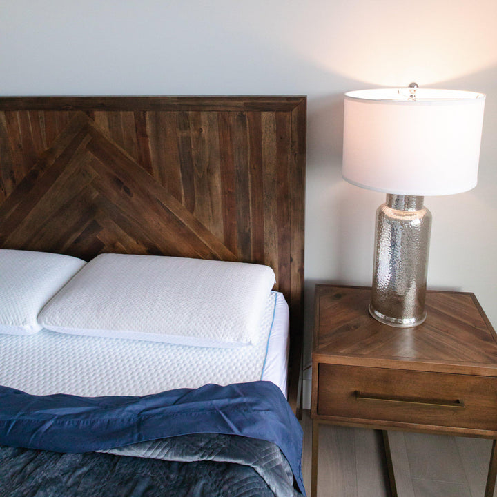 showcase of Bedface Artic Cooling Pillow protector and mattress protector covering a memory foam pill and Haven Mattress with blue bedding folding down with a wooden headboard and side table with lamp