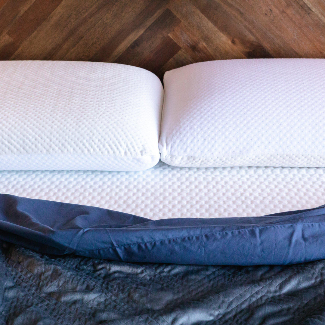 close up of two memory foam pillows covered with Bedface artic cooling pillow protectors on a artic cooling mattress protector, blue bedding folding down and a wooden headboard in background